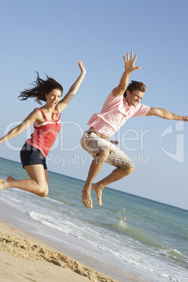 Young Couple Enjoying Beach Holiday Jumping In Air