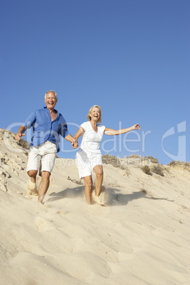 Senior Couple Enjoying Beach Holiday Running Down Dune