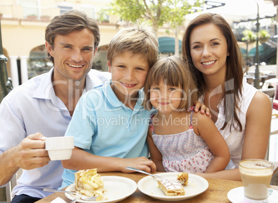 Young Family Enjoying Cup Of Coffee And Cake In Caf? Together