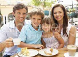 Young Family Enjoying Cup Of Coffee And Cake In Caf? Together