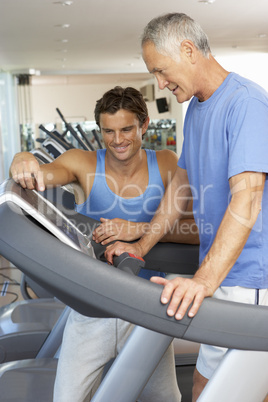 Man Working With Personal Trainer On Running Machine In Gym