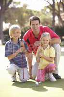 Father Teaching Children To Play Golf On Putting On Green