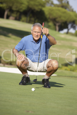 Senior Male Golfer On Golf Course Lining Up Putt On Green