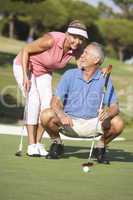 Senior Couple Golfing On Golf Course Lining Up Putt On Green