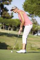 Senior Female Golfer On Golf Course Lining Up Putt On Green