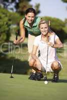 Two Female Golfers On Golf Course Lining Up Putt On Green