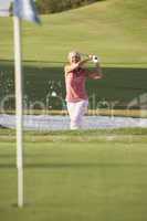 Senior Female Golfer Playing Bunker Shot On Golf Course