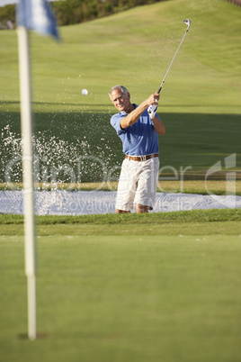 Senior Male Golfer Playing Bunker Shot On Golf Course