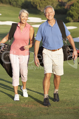 Senior Couple Walking Along Golf Course Carrying Bags