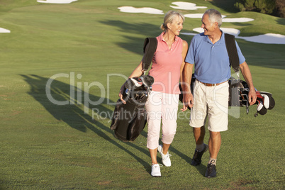 Senior Couple Walking Along Golf Course Carrying Bags