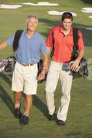 Two Men Walking Along Golf Course Carrying Bags