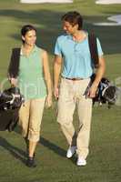 Couple Walking Along Golf Course Carrying Bags