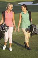 Two Women Walking Along Golf Course Carrying Bags