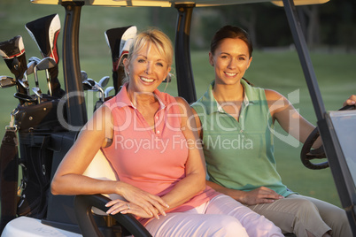 Two Female Golfers Riding In Golf Buggy On Golf Course