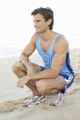 Young Man In Fitness Clothing Resting After Exercise On Beach