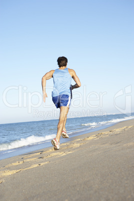 Young Man In Fitness Clothing Running Along Beach