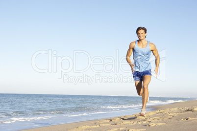 Young Man In Fitness Clothing Running Along Beach