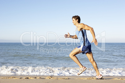 Young Man In Fitness Clothing Running Along Beach