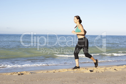 Young Woman In Fitness Clothing Running Along Beach