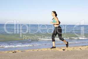 Young Woman In Fitness Clothing Running Along Beach