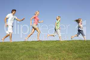 Young family, parents with children,  running through field