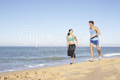 Young Couple In Fitness Clothing Running Along Beach