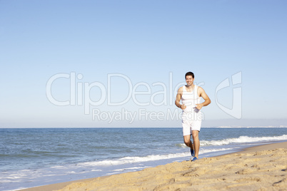 Young Man In Fitness Clothing Running Along Beach