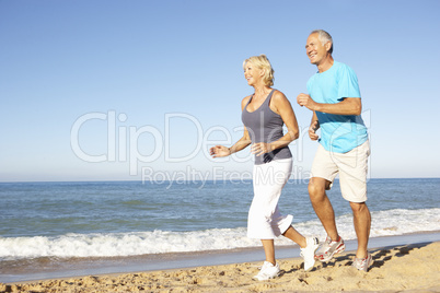 Senior Couple In Fitness Clothing Running Along Beach