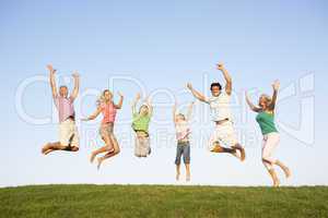 Young couple with grandparents and children jump in a field