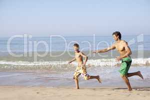 Father chasing young boy on beach