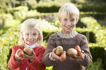 Young children in garden pose with vegetables