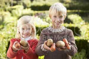 Young children in garden pose with vegetables