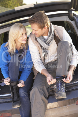 Young couple tie boots at rear of car