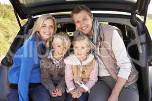 Young family pose together at rear of car