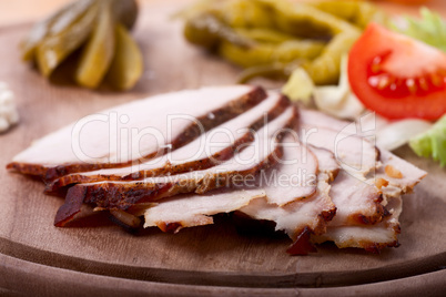 Scheiben von kaltem Schweinebraten auf einem Holzteller