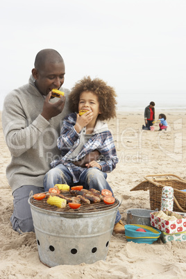 Young Family Enjoying Barbeque On Beach