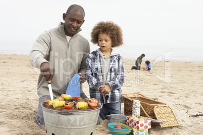 Young Family Enjoying Barbeque On Beach
