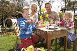 Family Decorating Easter Eggs On Table Outdoors