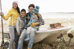 Family Group Sitting On Boat With Fishing Rod On Winter Beach