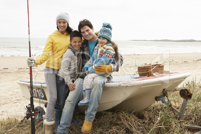 Family Group Sitting On Boat With Fishing Rod On Winter Beach