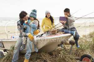 Family Group Sitting On Boat With Fishing Rod On Winter Beach