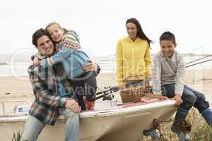 Family Group Sitting On Boat With Fishing Rod On Winter Beach