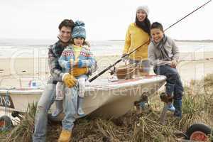 Family Group Sitting On Boat With Fishing Rod On Winter Beach