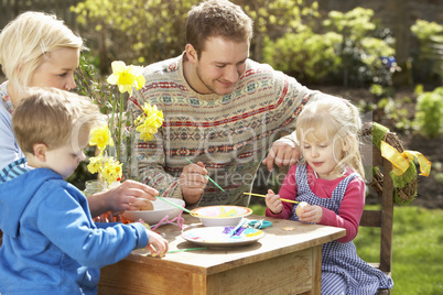 Family Decorating Easter Eggs On Table Outdoors