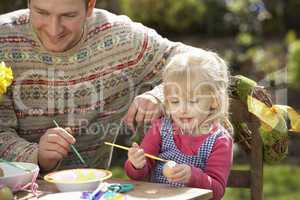 Father And Daughter Decorating Easter Eggs On Table Outdoors