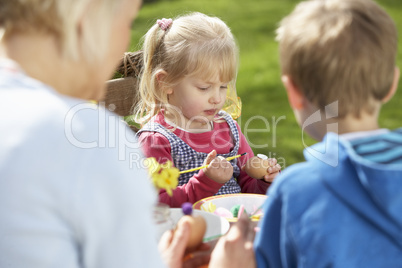 Mother And Children Decorating Easter Eggs On Table Outdoors