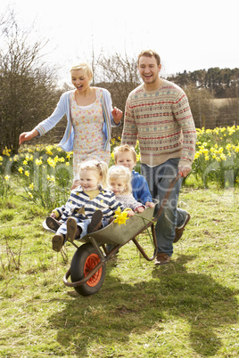 Father Giving Children Ride In Wheelbarrow Through Field Of Spri