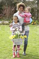 Mother And Children Holding Basket Of Daffodils In Garden