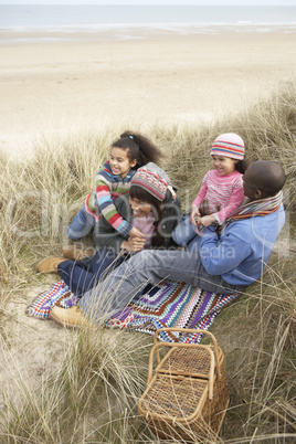 Family Sitting In Dunes Enjoying Picnic On Winter Beach