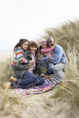 Family Sitting On Blanket In Dunes On Winter Beach
